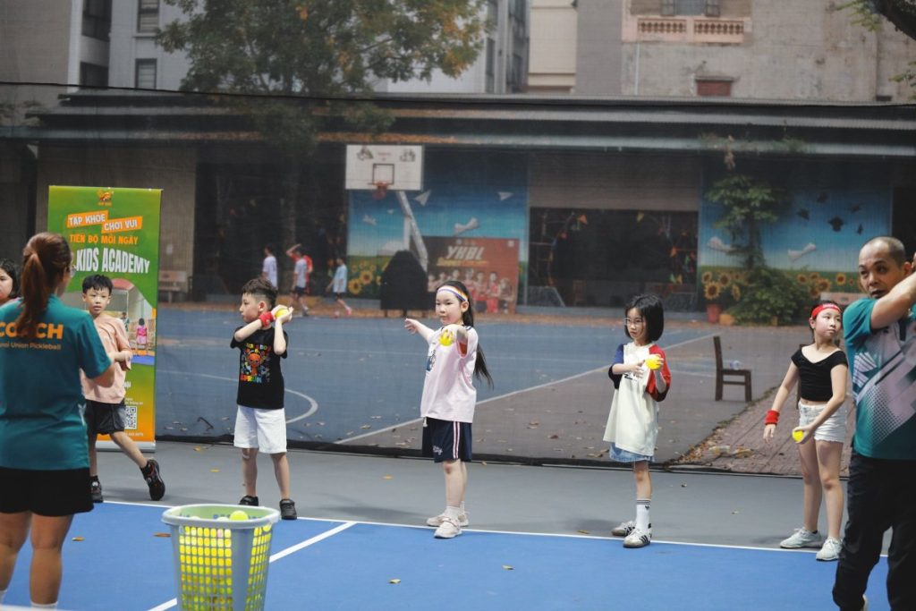 Các em nhỏ tham gia lớp học Pickleball Kid tại Hà Nội đang chăm chú lắng nghe huấn luyện viên hướng dẫn kỹ thuật trên sân tập.